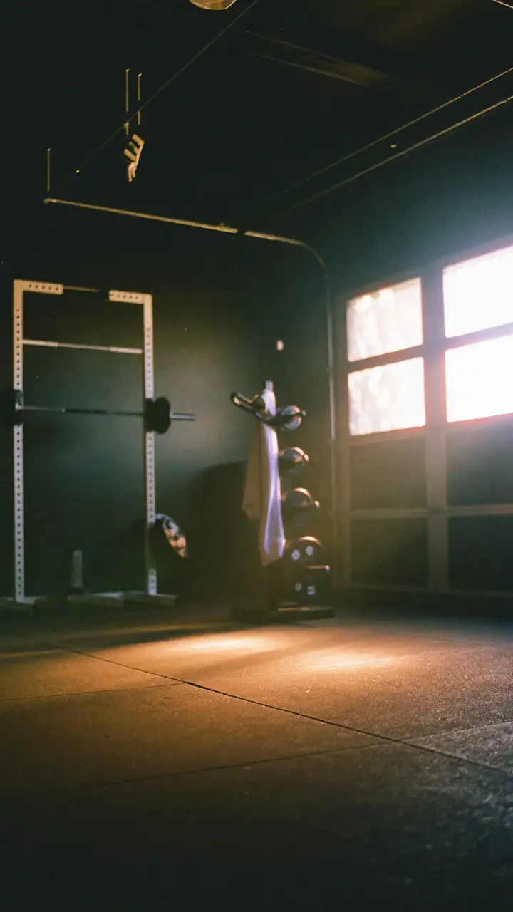 A garage gym at first light, the door part open, a barbell on a squat rack.